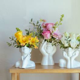 Three small floral arrangements in white face-shaped vases on a wooden table
