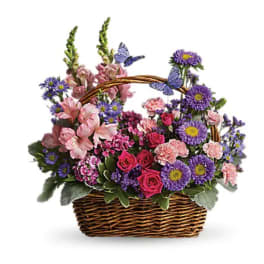 Basket arrangement of pink roses and carnations with purple asters and faux butterflies