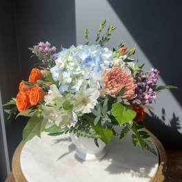 Mixed bouquet in a white vase with blue hydrangea, orange roses, and pink blooms