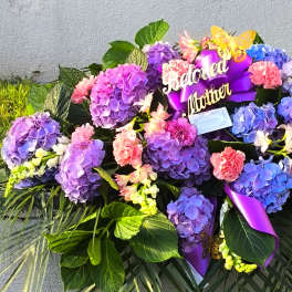 Large floral arrangement with purple hydrangeas, pink carnations, and a purple ribbon