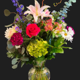 Mixed bouquet with a pink lily, red rose, and daisies in a glass vase