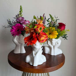 Three colorful flower arrangements in white face-shaped vases on a round table