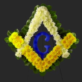 Diamond-shaped floral wreath with white and yellow flowers around a blue letter G