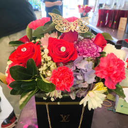 Bright mixed flower arrangement in a black gift box with a gold butterfly topper