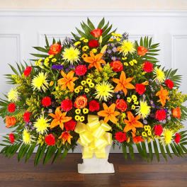 Large colorful floral spray with orange lilies and roses in a white pedestal vase