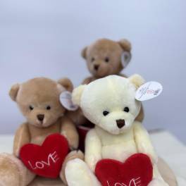 Three teddy bears holding red hearts on a round wooden base
