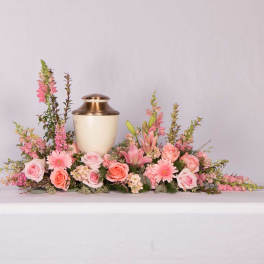 Pink floral arrangement surrounding a gold urn