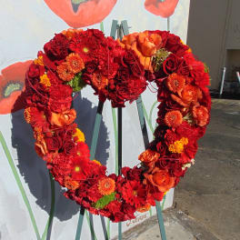 Heart-shaped standing wreath of red and orange roses, gerbera daisies, and mums on a metal easel