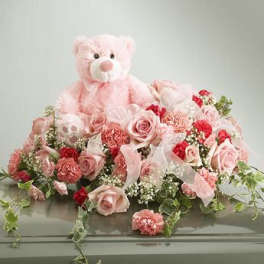 Pink teddy bear surrounded by pink and red flowers