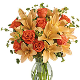 Orange roses and pale lilies in a clear glass vase