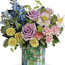 Mixed bouquet of roses, lilies, and blue flowers in a mosaic vase