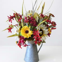 Mixed bouquet of daisies and red flowers in a metal pitcher