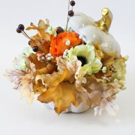 Orange and cream floral arrangement in a white pumpkin container