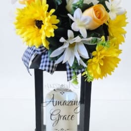 Yellow and white floral arrangement in a black lantern with a candle
