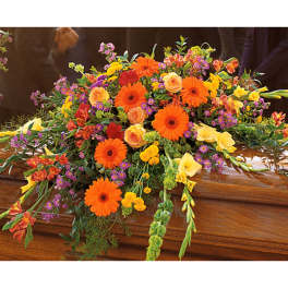 Colorful floral casket spray with orange gerberas, yellow callas, and purple accents