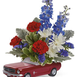 Floral arrangement in a red toy car container with red, white, and blue flowers