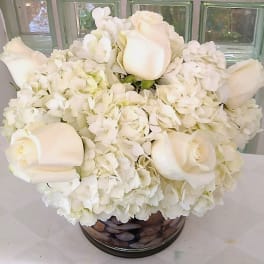 White roses and hydrangeas arranged in a round glass vase