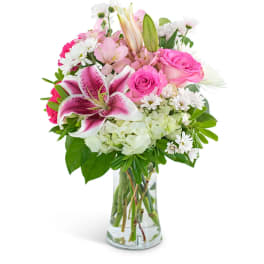 Pink lilies, roses, and white mixed flowers arranged in a clear glass vase
