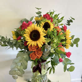 Bouquet of sunflowers, orange roses, and pink carnations in a glass vase