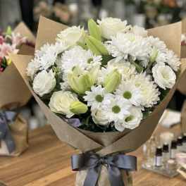 White bouquet with lilies, roses, and daisies wrapped in brown paper