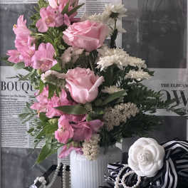 Pink and white floral arrangement in a white vase with ribbon accents