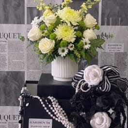 White and pale yellow flower arrangement in a white vase with black ribbon accessories