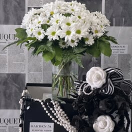 White daisy bouquet in a clear glass vase with black-and-white ribbon accents
