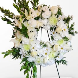 White floral wreath on a stand with lilies, roses, and daisies