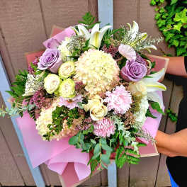Hand-tied bouquet of pastel roses, lilies, and hydrangeas wrapped in pink paper