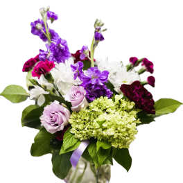 Mixed bouquet of purple, white, and green flowers in a glass vase