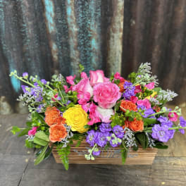 Low wooden box filled with bright pink roses, yellow and orange blooms, and purple flowers