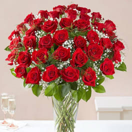 Tall clear vase filled with many red roses and white filler flowers on a white table