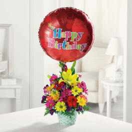 Bright mixed flower arrangement in a glass vase with a red Happy Birthday balloon.