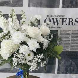 White floral bouquet in a glass vase with a blue ribbon