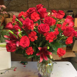 Tall arrangement of red roses, carnations, and lilies in a clear glass vase