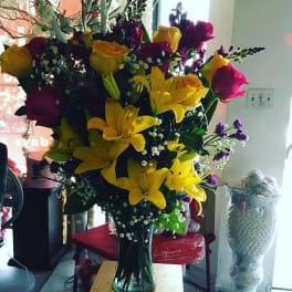 Tall bouquet of yellow lilies and mixed roses in a clear glass vase
