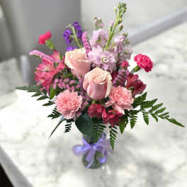 Pink and purple mixed bouquet in a glass vase with a lavender ribbon