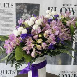 Pink alstroemeria and white pompom flowers in a white vase with a purple ribbon