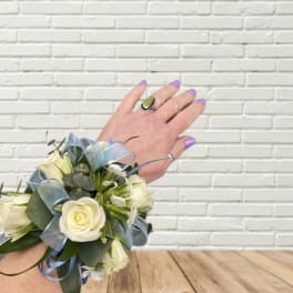 White rose wrist corsage with blue ribbon on a person's wrist