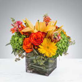 Bright mixed bouquet with roses and lilies in a square glass vase
