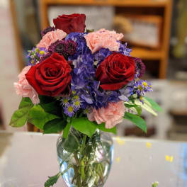 Bouquet of red roses, pink carnations, and blue hydrangeas in a glass vase