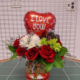 Red roses and white flowers in a glass vase with a heart balloon