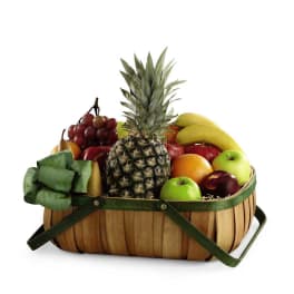 Wooden basket filled with assorted fresh fruits including pineapple, bananas, and apples