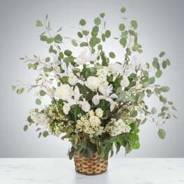 White flowers and roses arranged in a woven basket with tall eucalyptus branches