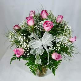 Pink roses in a clear vase with white baby's breath and a white ribbon bow