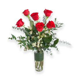 Red roses arranged in a clear glass vase with greenery