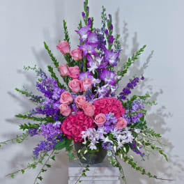 Tall arrangement of pink roses and purple flowers in a dark vase