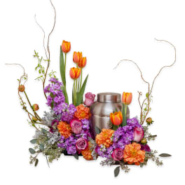 Orange tulips and purple flowers arranged around a silver urn