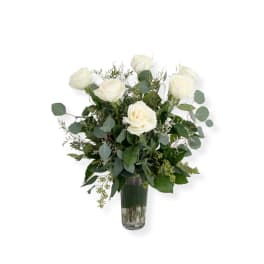 White roses in a clear glass vase with mixed greenery