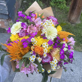 Mixed bouquet with roses, daisies, and bright orange accents in brown paper